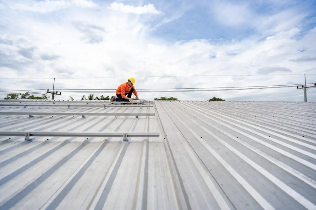 Technician in safety uniform and helmet kneeling on a rooftop, using a drill for precise installation work. A scene highlighting safety, professionalism, and technical expertise in construction.