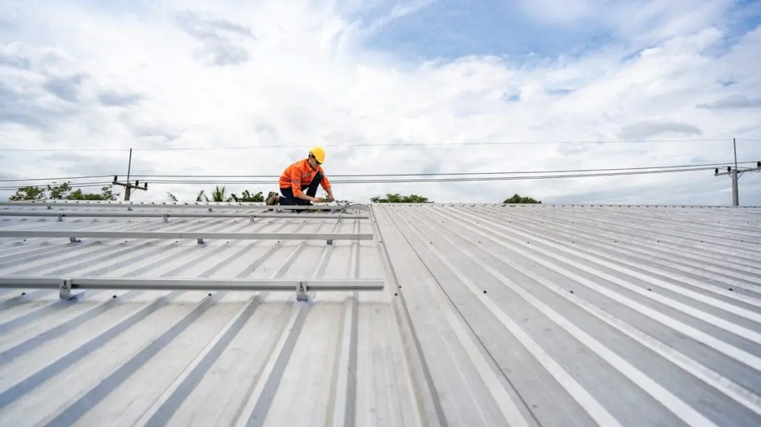 Technician in safety uniform and helmet kneeling on a rooftop, using a drill for precise installation work. A scene highlighting safety, professionalism, and technical expertise in construction.